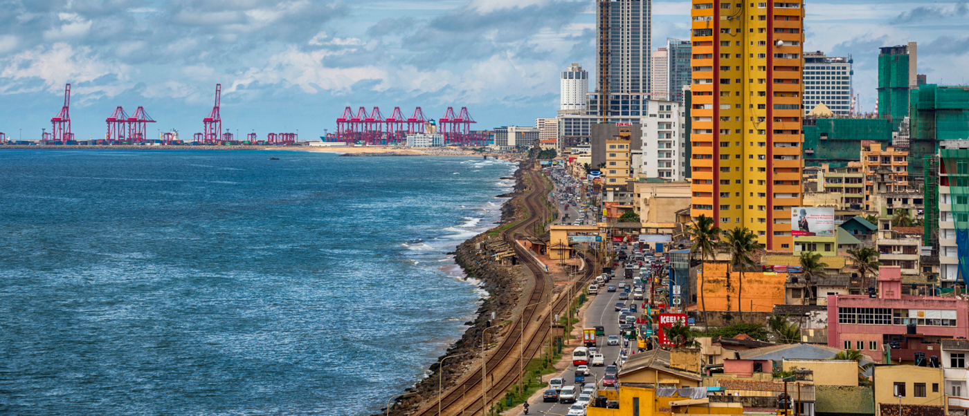 Colombo's bustling coastline with a busy road, colorful buildings, and numerous port cranes.