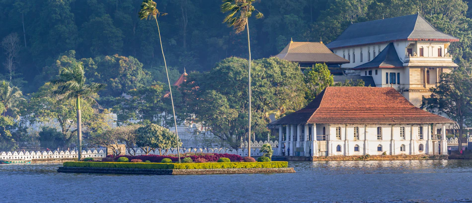 Serene Kandy Lake with the Temple of the Tooth Relic and lush green hills.