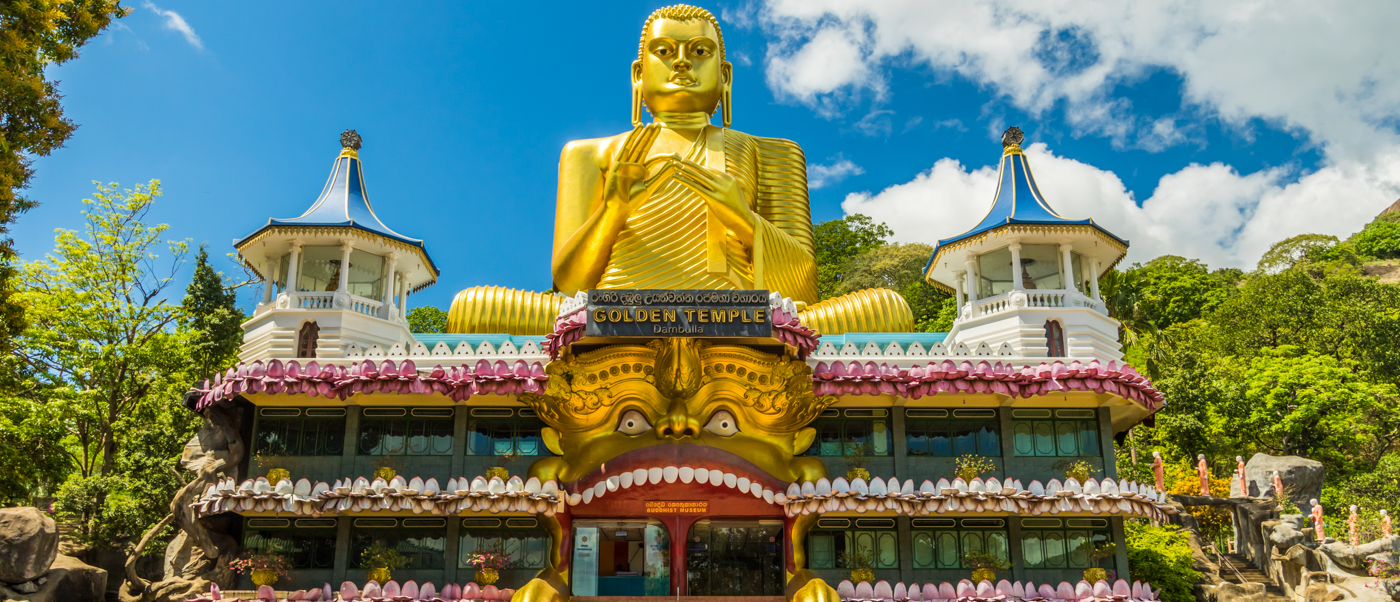 A colossal golden Buddha statue overlooks the ornate Golden Temple building in Dambulla, Sri Lanka.