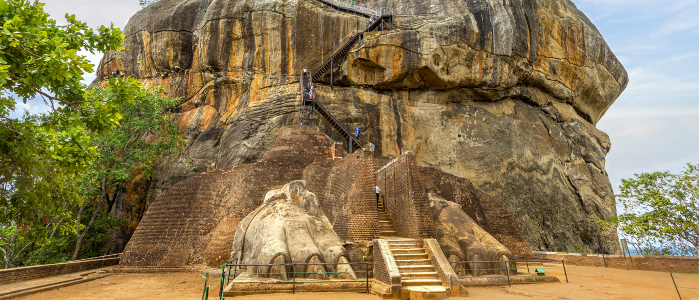 Tourists climb the grand staircase and metal steps carved into the base of Sigiriya Lion Rock.