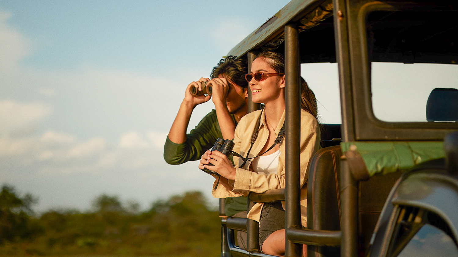 A happy couple enjoys a jeep safari in Yala National Park, spotting wildlife with binoculars.
