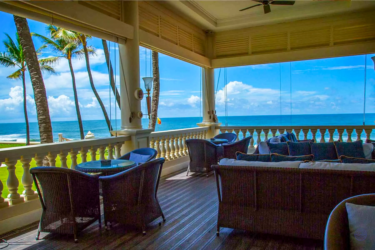 Elegant Galle Face Hotel balcony with comfortable seating overlooking the blue ocean and palm trees.
