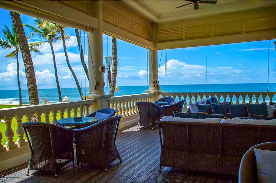 Elegant Galle Face Hotel balcony with comfortable seating overlooking the blue ocean and palm trees.