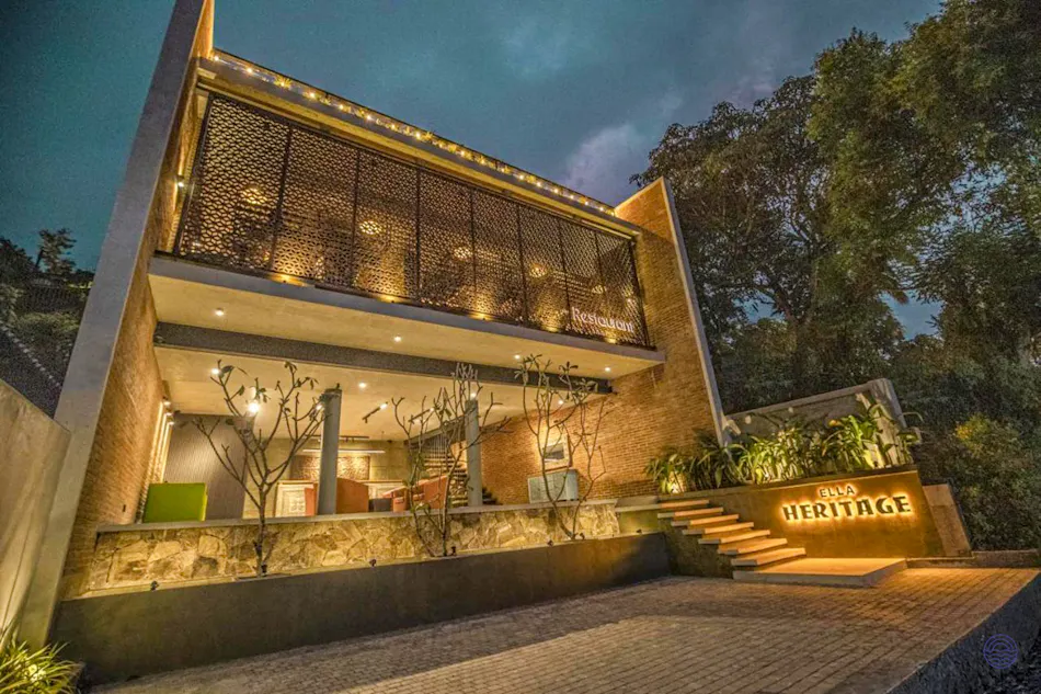 Modern Ella Heritage hotel at dusk, featuring a lit sign, stairs, and lush trees.