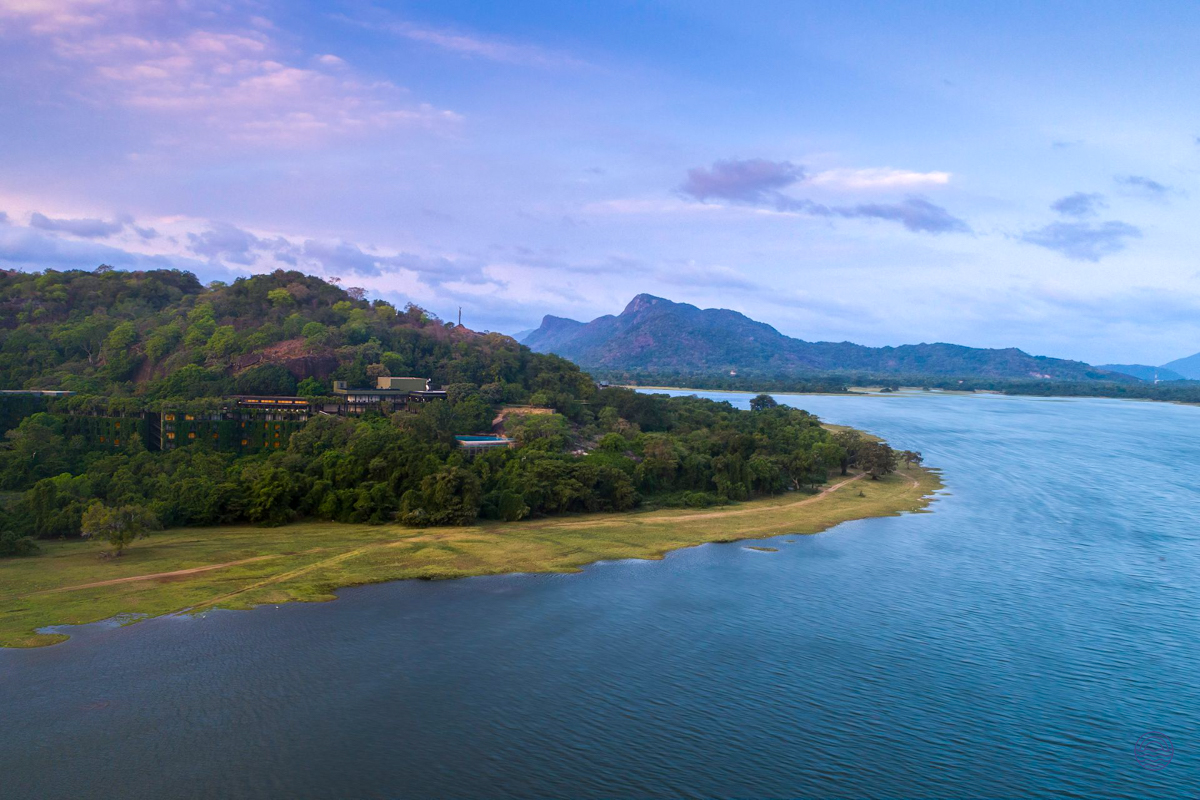 Heritance Kandalama hotel nestled in lush green trees beside Kandalama Lake at dusk.