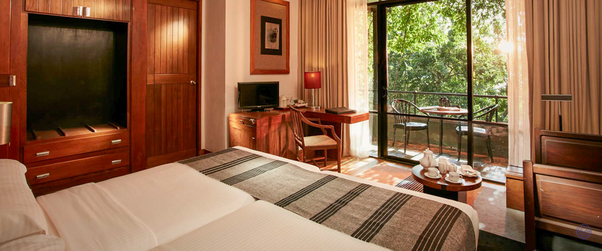 A comfortable hotel room with twin beds and a private balcony overlooking lush greenery in Sigiriya.
