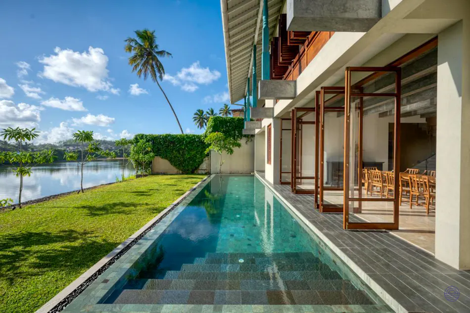 Modern resort building with a long pool, green lawn, and serene lake in Weligama.
