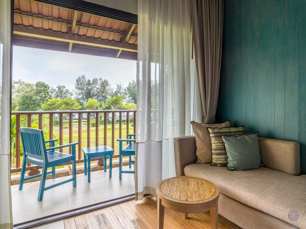 Inviting hotel room with a comfortable chaise lounge and a balcony offering a serene green garden view.