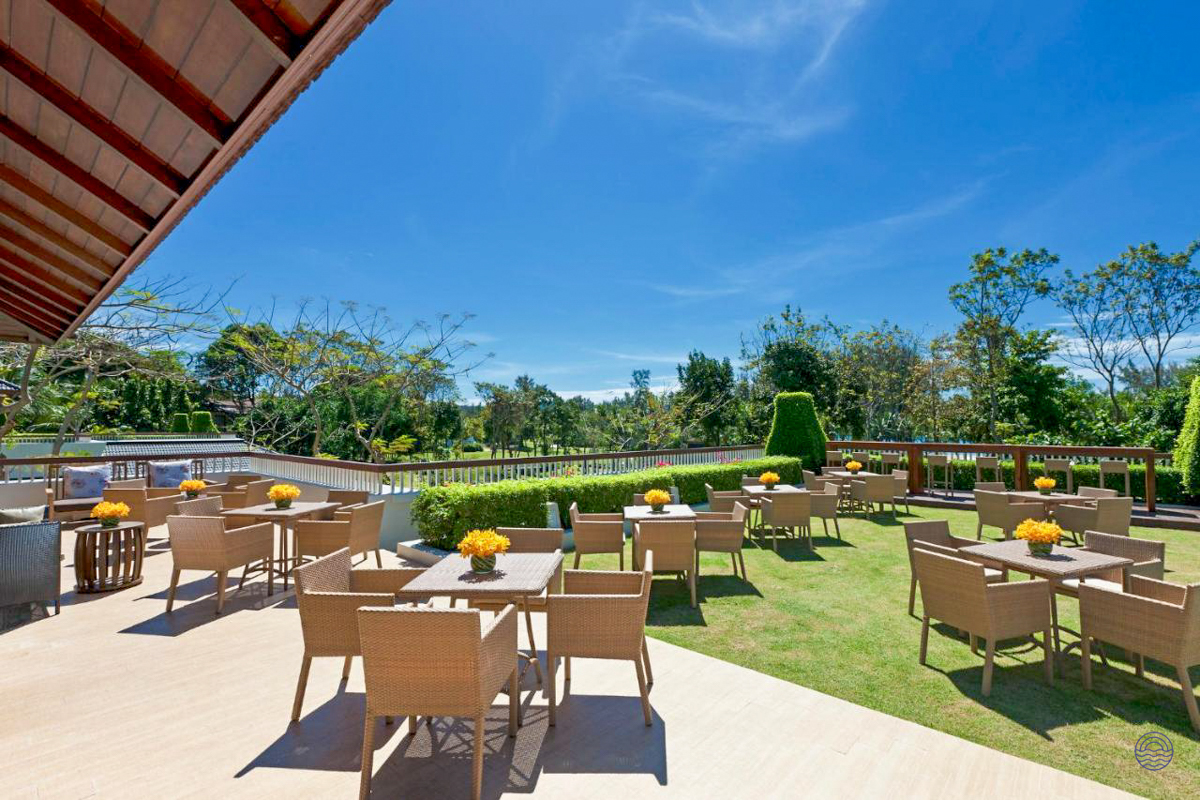 Outdoor dining area at Dusit Thani Krabi, featuring a patio, green lawn, and bright blue sky.