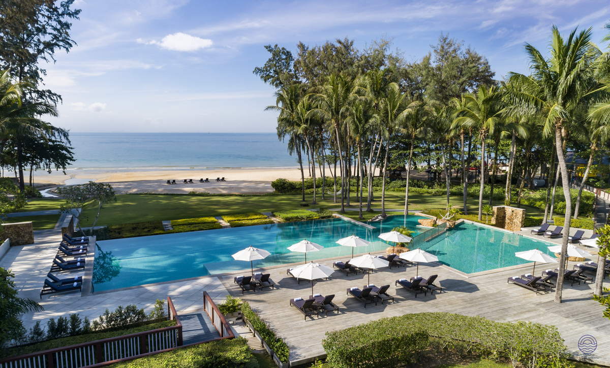 Luxurious resort swimming pool with lounge chairs, palm trees, and a sandy beach in Krabi, Thailand.