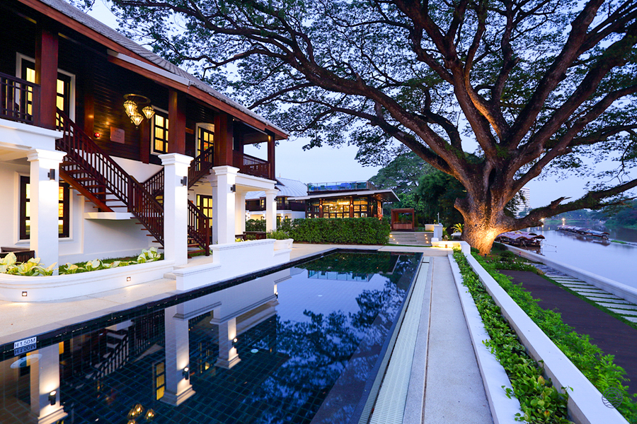 Stunning historical resort in Chiang Mai with a beautiful pool and traditional architecture by the river at dusk.