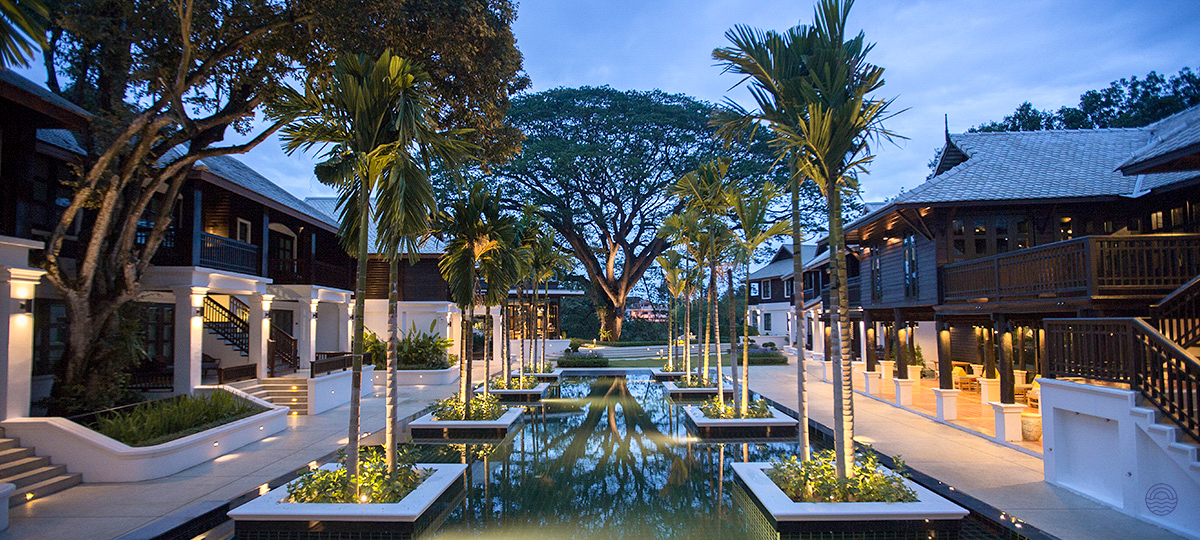 Elegant traditional Thai resort in Chiang Mai at twilight, with reflective water gardens and palm trees.