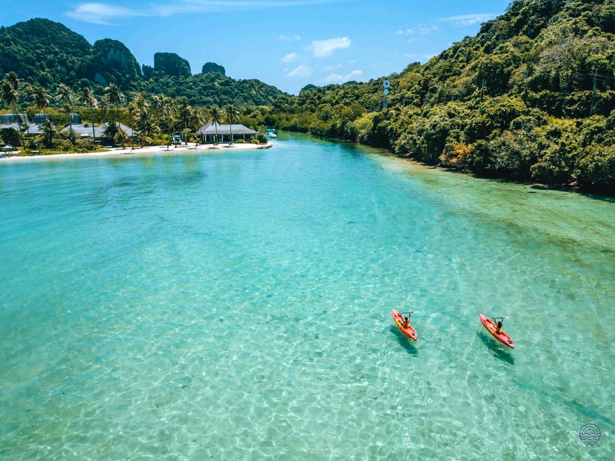 Two red kayaks glide across the pristine turquoise waters of Koh Phi Phi, surrounded by lush tropical islands.