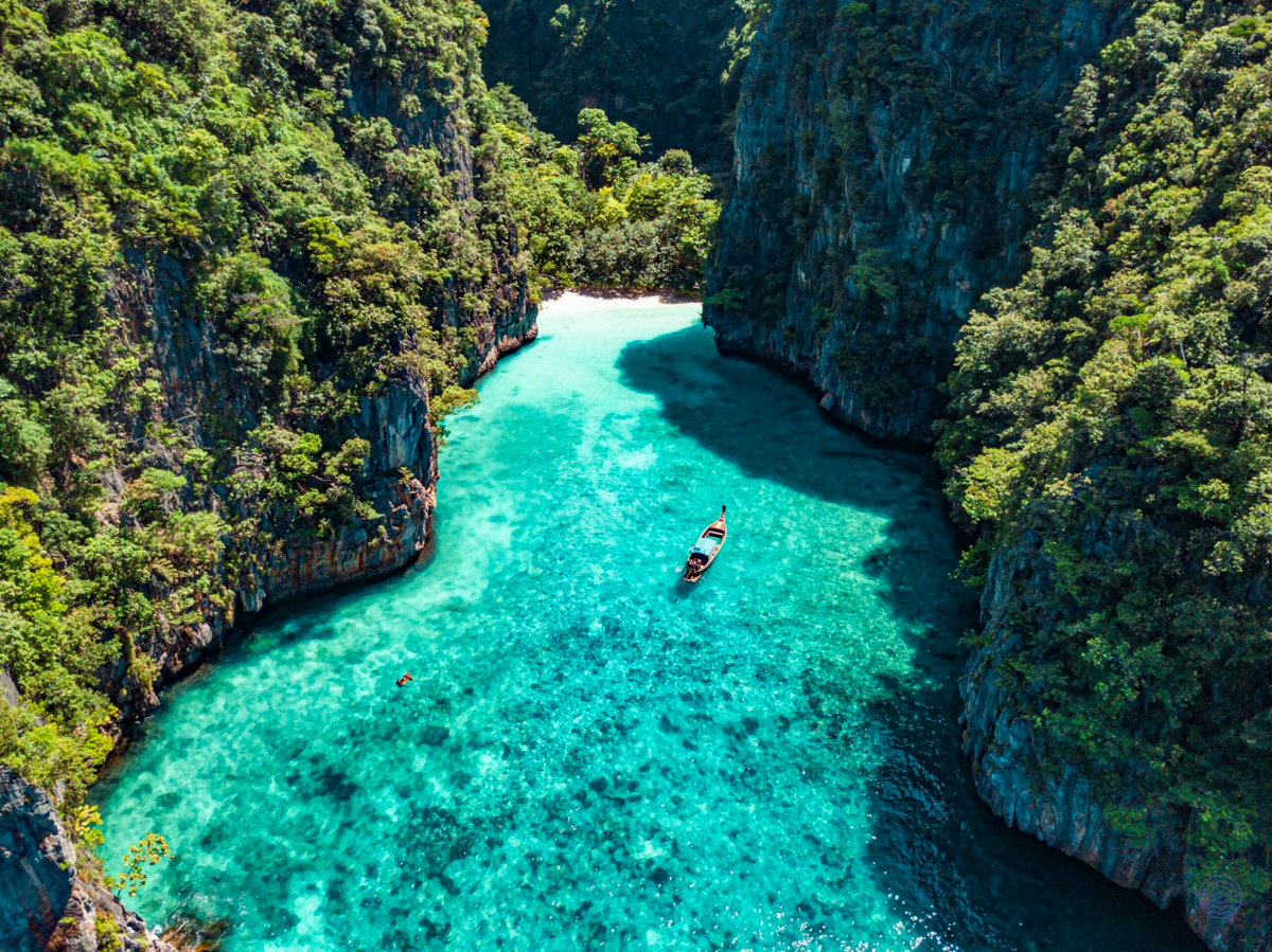 Serene turquoise cove with a longtail boat, surrounded by lush green cliffs at Koh Phi Phi.