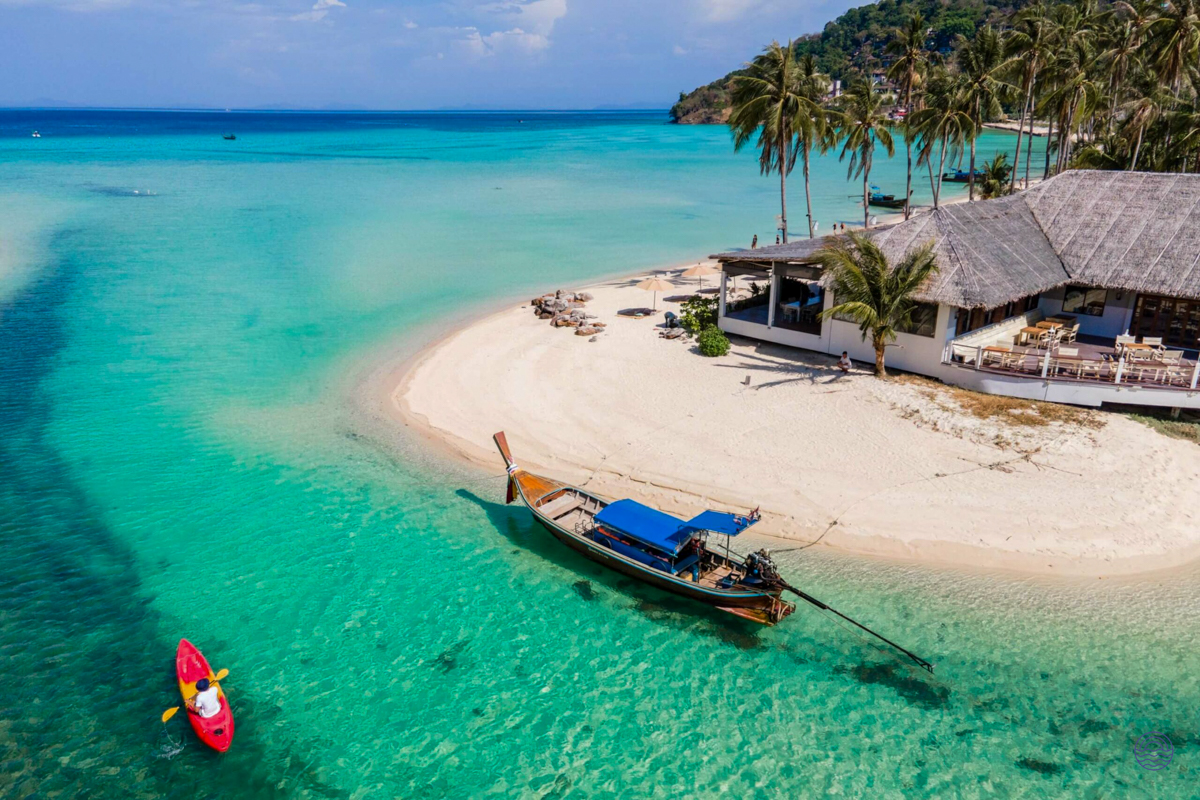 A traditional longtail boat floats in clear turquoise water by a white sand beach, Koh Phi Phi.