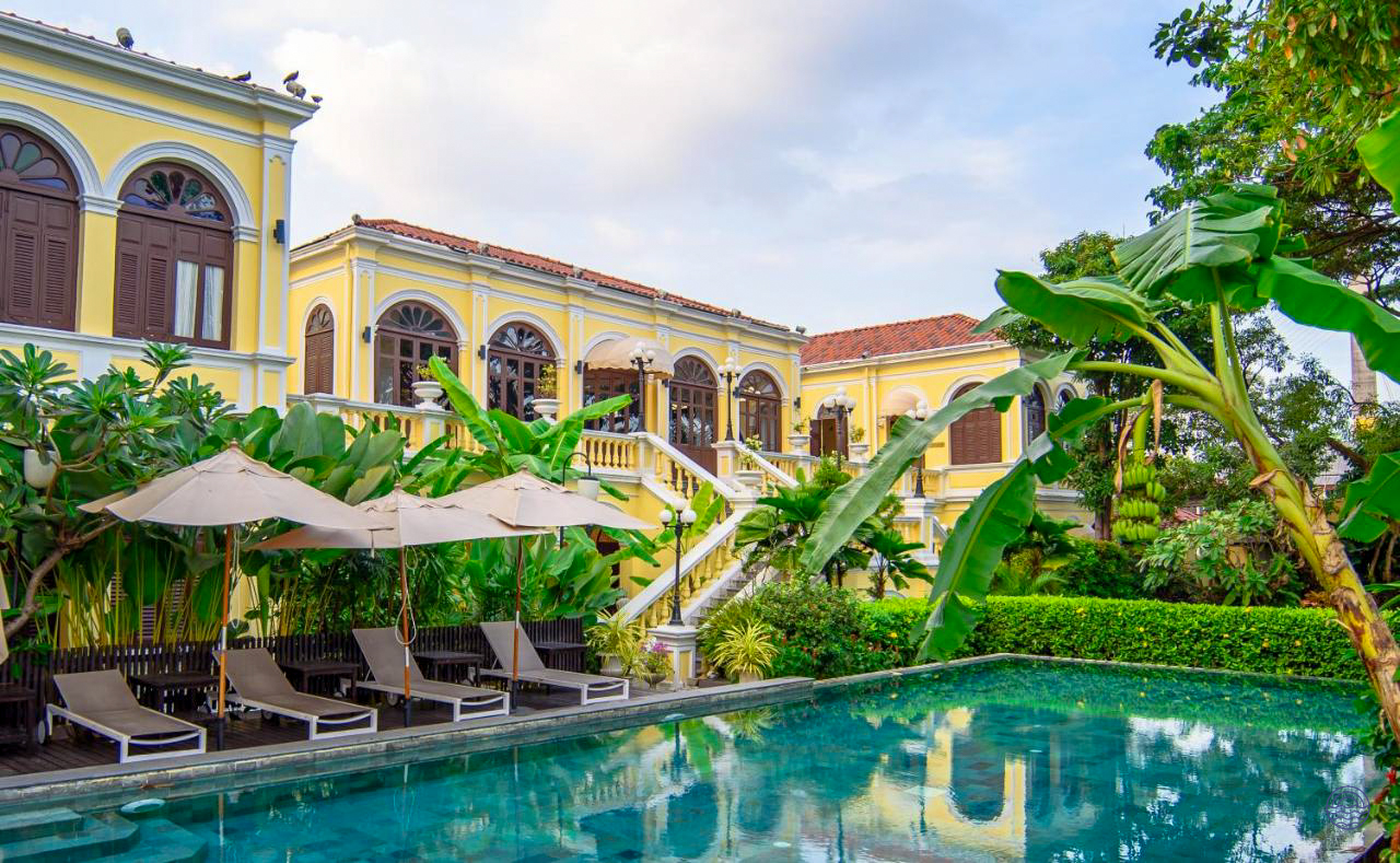 Relax by the refreshing pool at this elegant yellow hotel surrounded by tropical greenery in Bangkok.