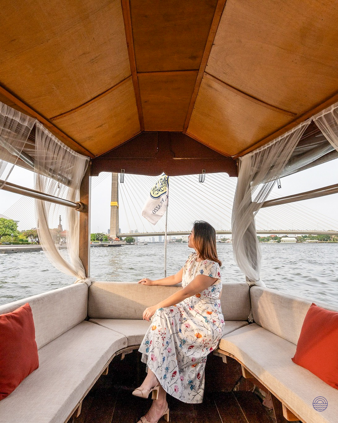 A woman in a floral dress relaxes on a boat ride, enjoying the scenic Chao Phraya River in Bangkok.