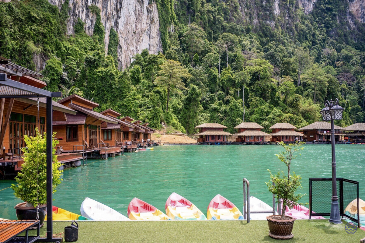 Floating bungalows on a calm turquoise lake, with kayaks and towering jungle-covered mountains in Khao Sok.