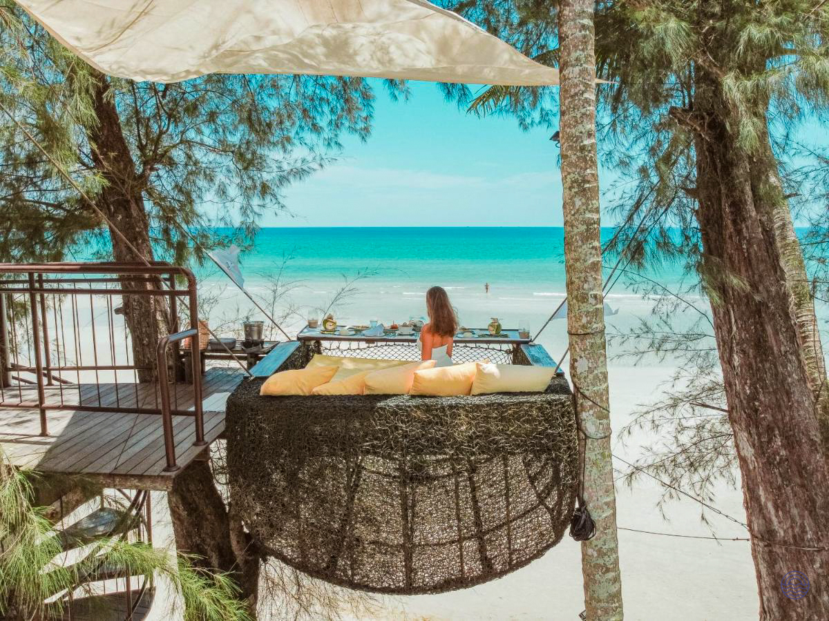 Woman relaxing in a luxurious hanging bed, enjoying the turquoise ocean view at Koh Kood.