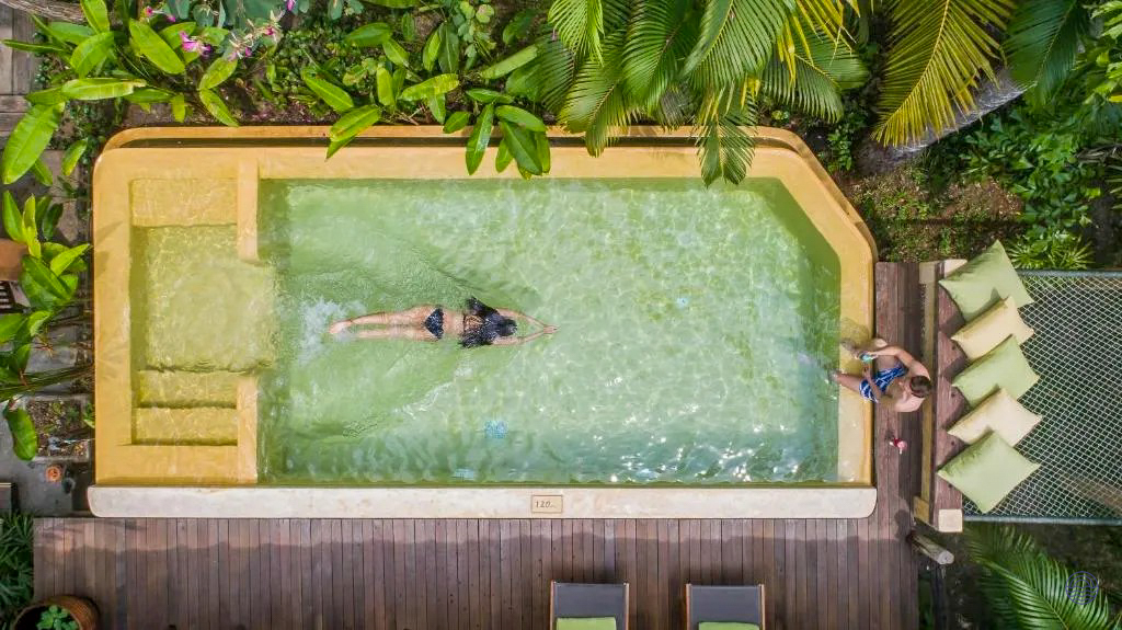 Overhead view of a private pool with a person swimming and another relaxing in tropical Koh Kood.