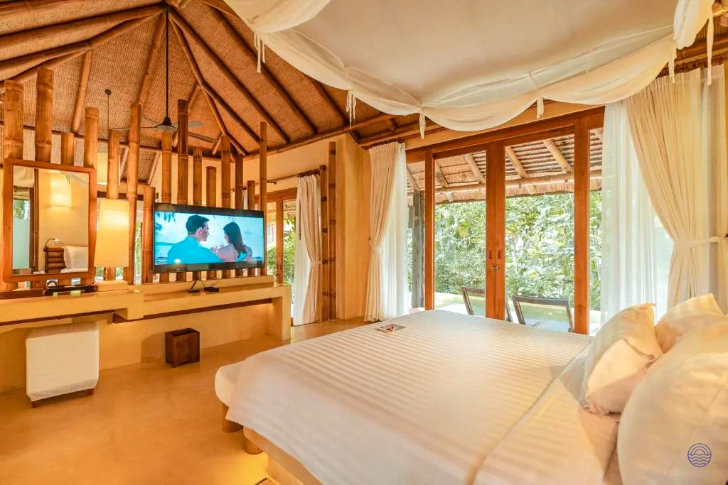 Spacious villa bedroom with a canopy bed and TV, overlooking lush tropical gardens in Koh Kood.