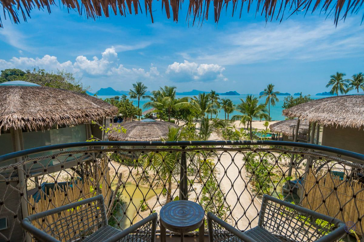 Balcony view from a treehouse villa at Koh Yao Noi, overlooking a tropical beach and turquoise ocean.