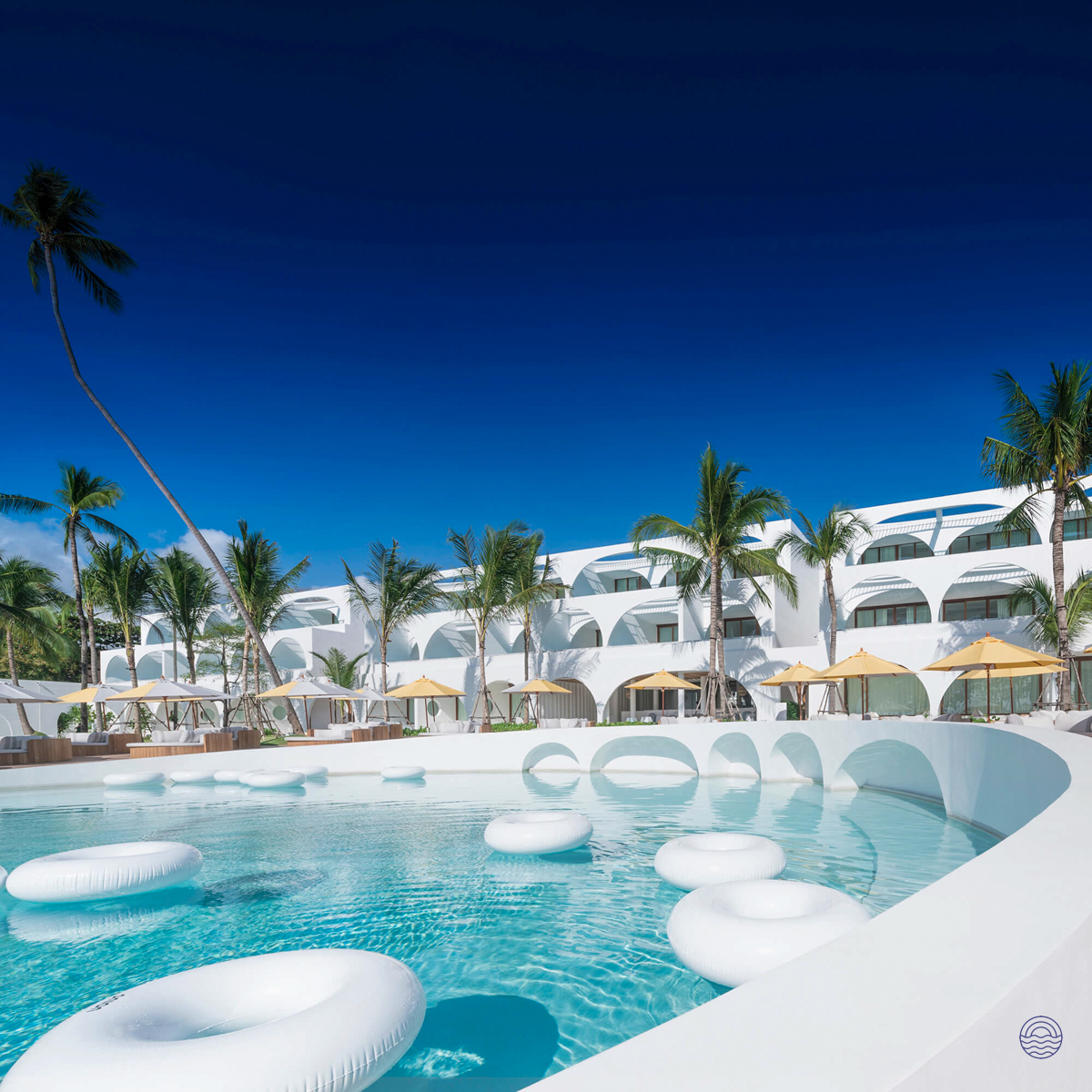 A stunning white resort with a large pool and palm trees under a clear blue sky in Koh Samui.