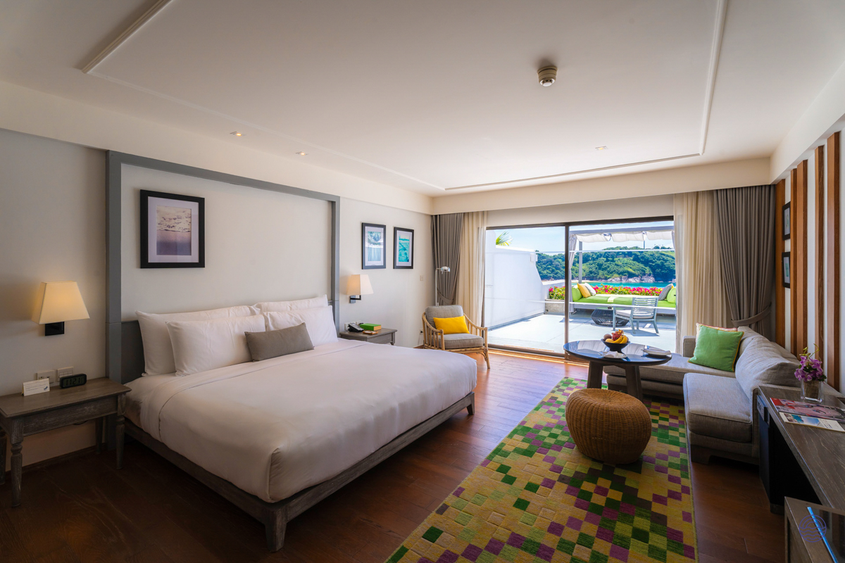 Luxurious hotel room in Phuket featuring a king bed, comfortable sofa, and a balcony with scenic views.