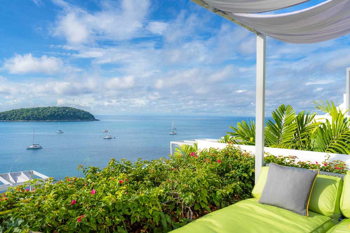 Luxurious balcony lounge with lush plants, overlooking the blue Phuket ocean and a distant tropical island.