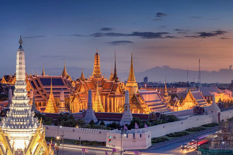 The magnificent Grand Palace in Bangkok glows golden at dusk, showcasing intricate Thai architecture.