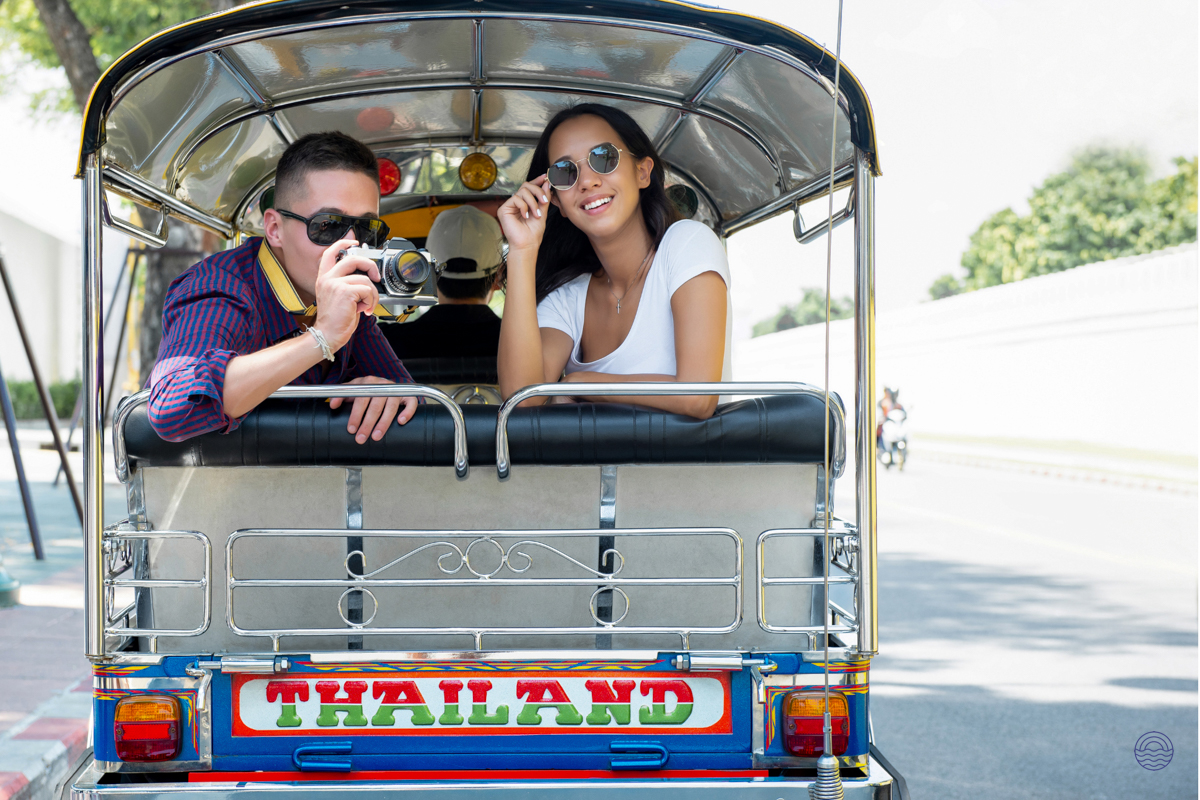 Smiling couple on a tuk-tuk in Bangkok, enjoying the sights and taking photos.
