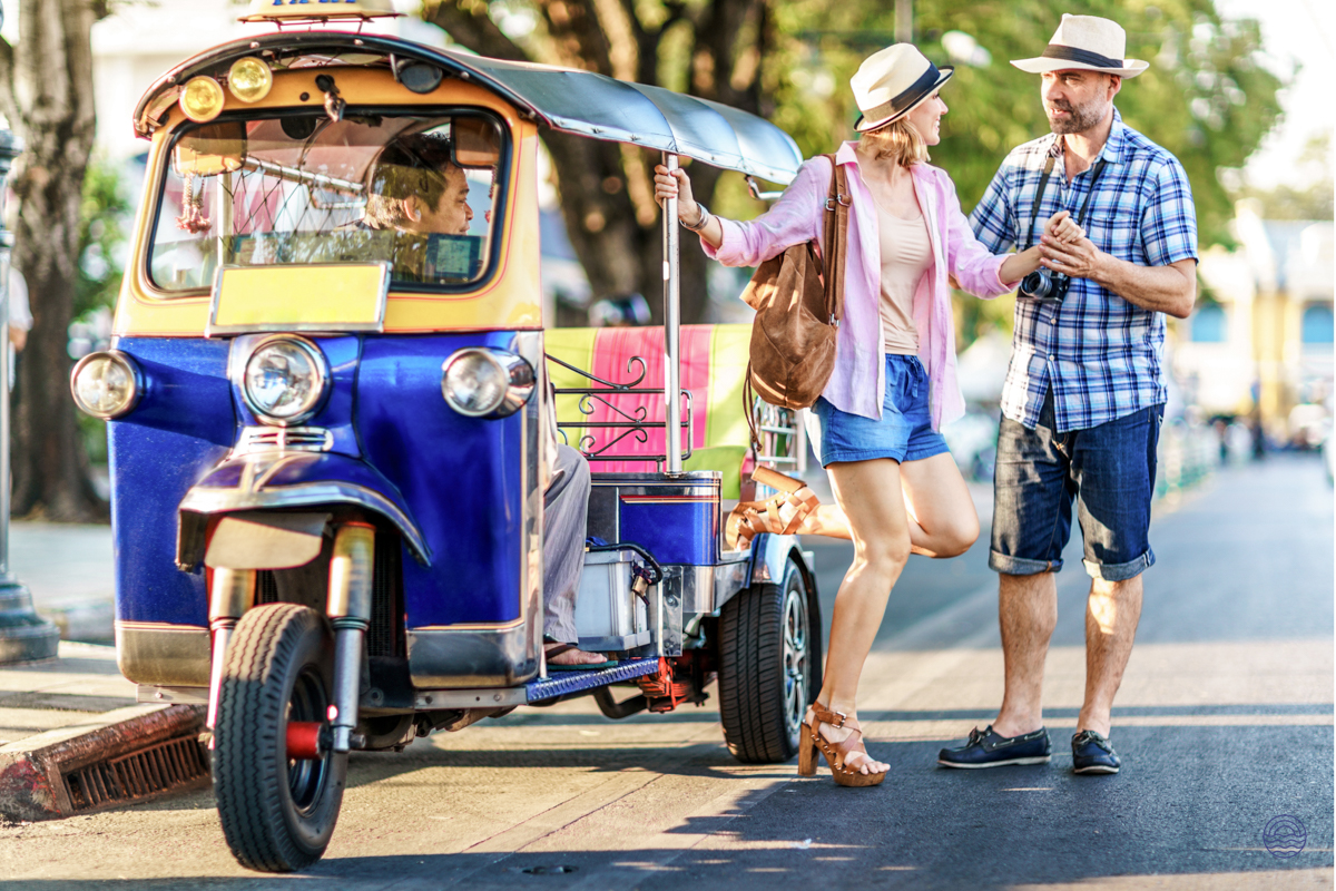 A couple chats next to a vibrant tuk-tuk, enjoying their tour through Bangkok.