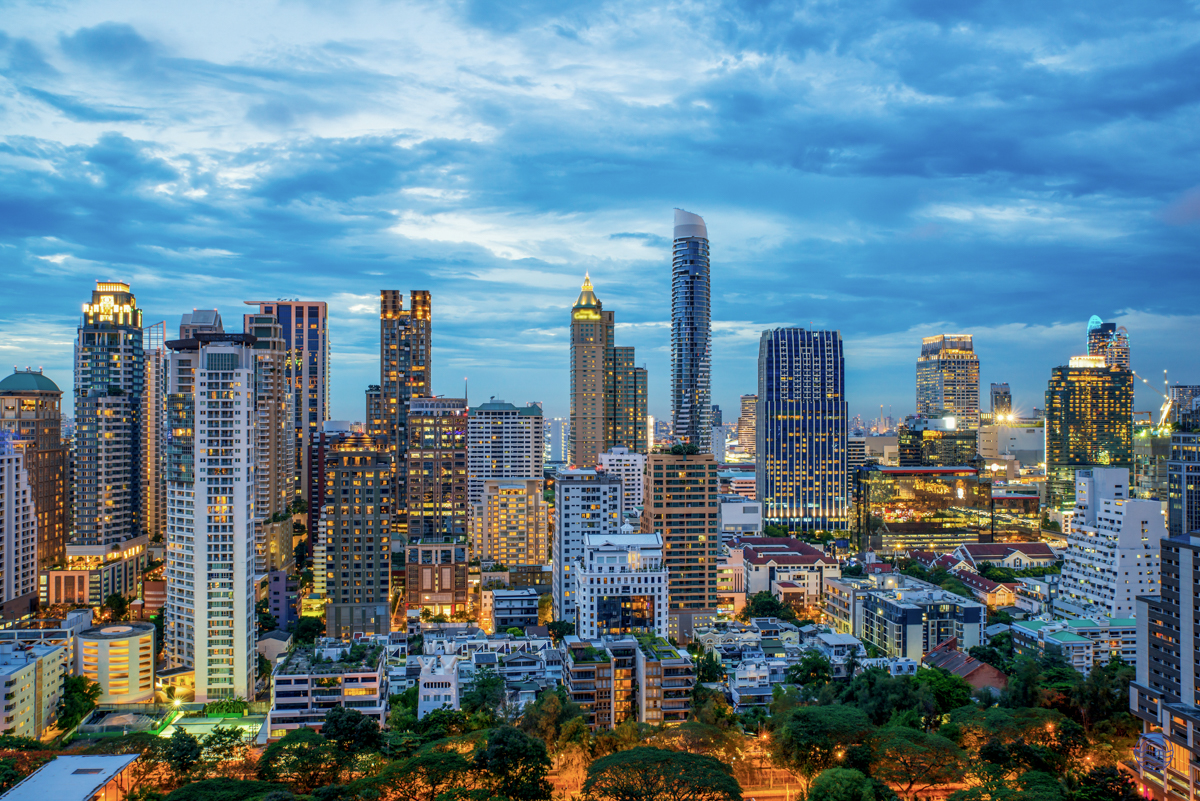 Bangkok's vibrant cityscape at dusk, featuring numerous illuminated skyscrapers under a dramatic sky.