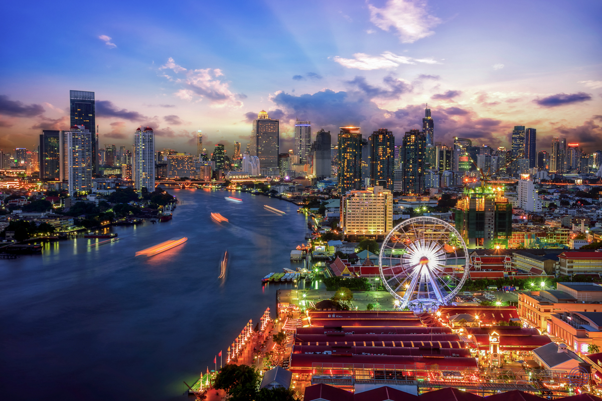 Vibrant Bangkok city at dusk, showing illuminated skyscrapers, river boats, and a prominent Ferris wheel.