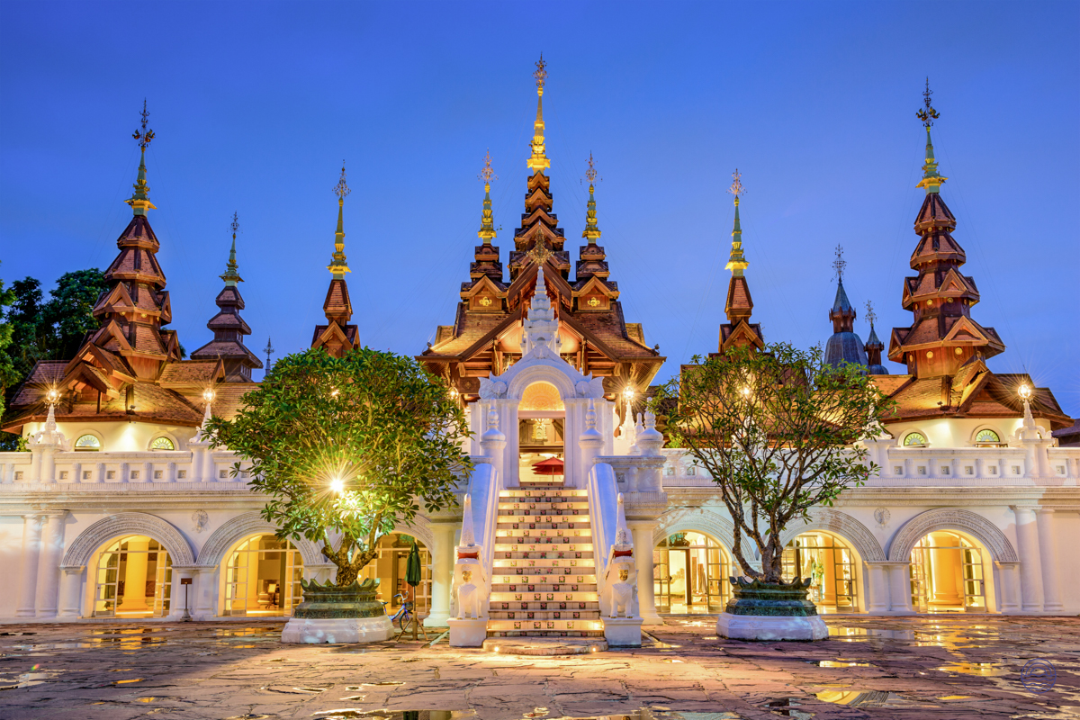 An ornate Thai temple in Chiang Mai glows beautifully at dusk, with golden spires and illuminated steps.