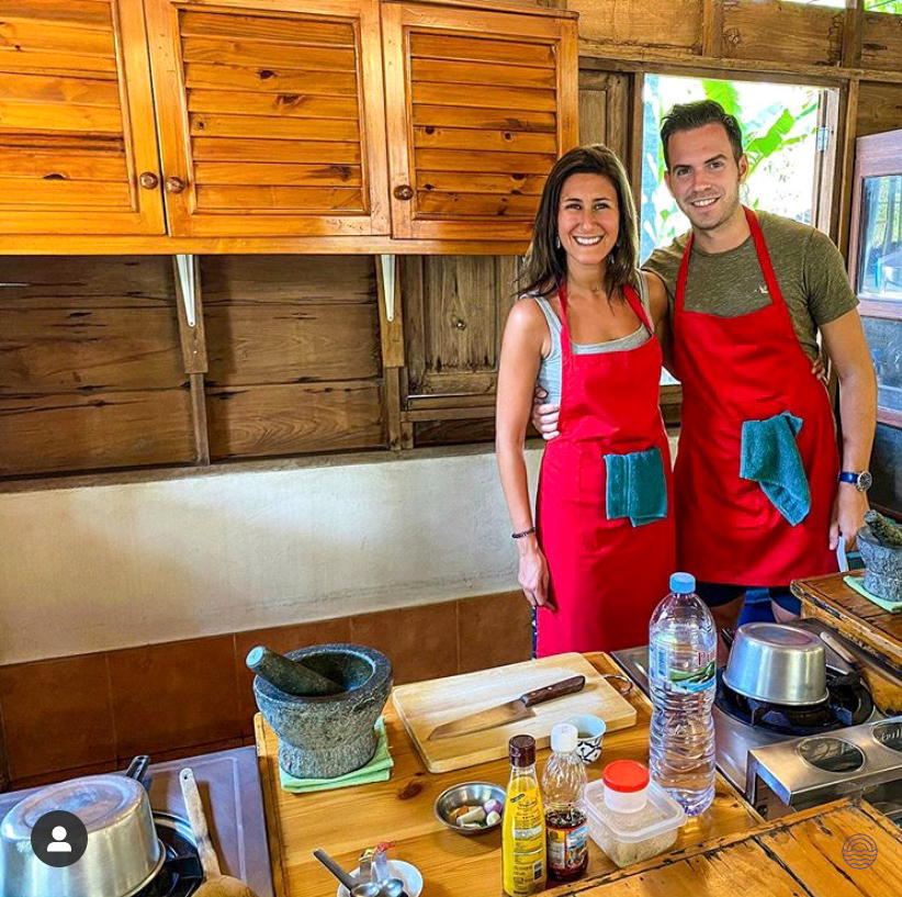 A happy couple in red aprons learning to cook traditional Thai dishes in Chiang Mai.