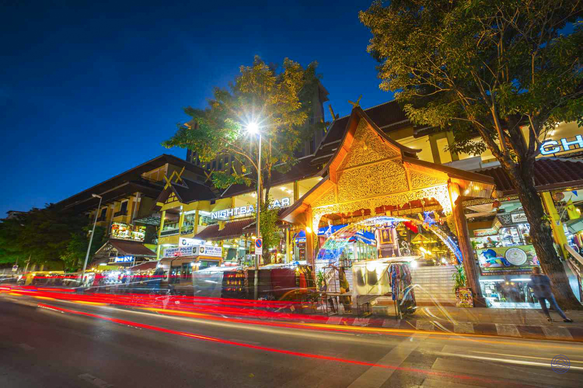 Vibrant night scene in Chiang Mai, featuring traditional Thai architecture and streaks of vehicle lights.
