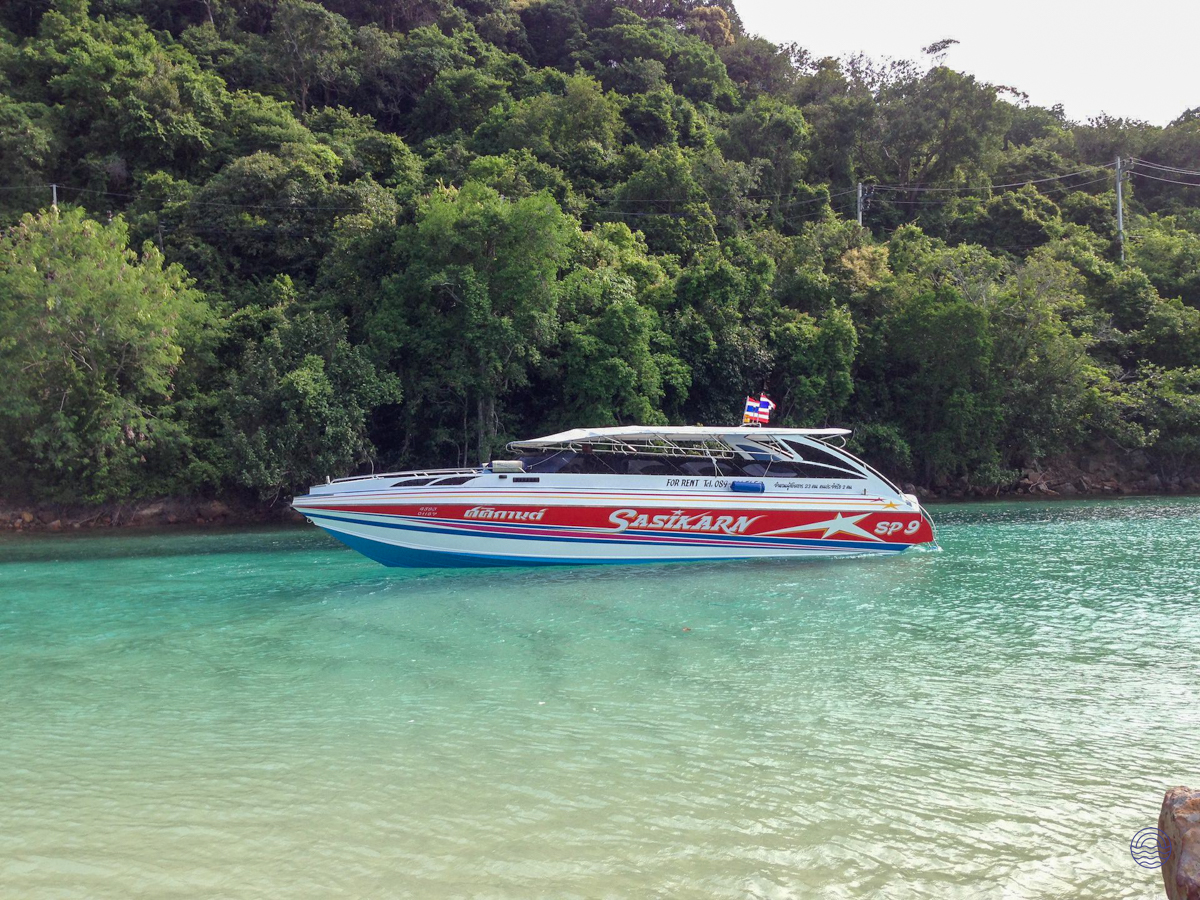 A red and white speedboat floats on turquoise water near lush green hills on Koh Phi Phi.