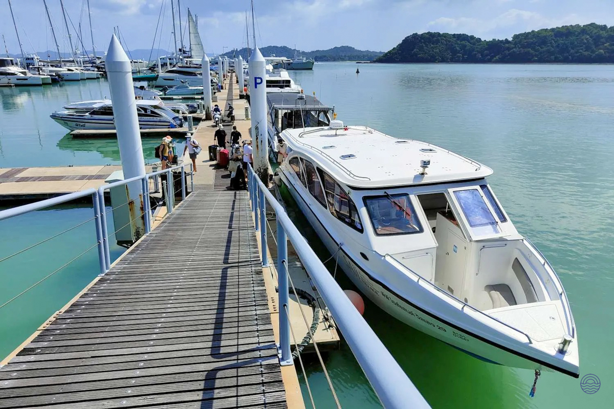 Passengers board a speedboat at a sunny pier in Koh Phi Phi, surrounded by clear turquoise waters.