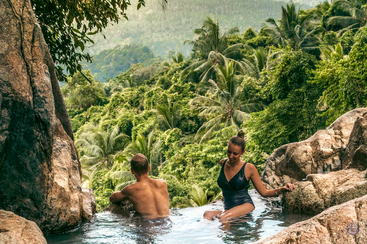 Couple relaxing in a natural pool with a stunning view of Koh Samui's tropical jungle.