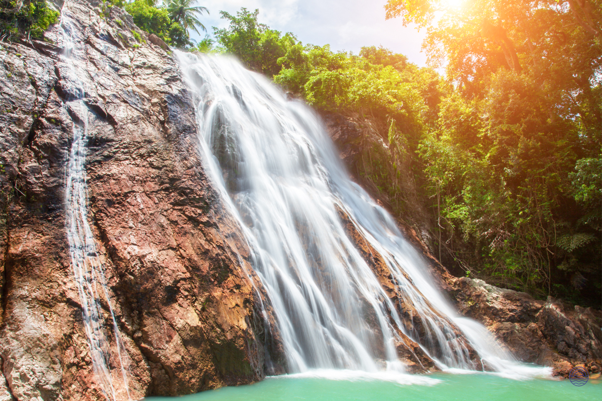 A stunning waterfall flows over a rocky cliff into a refreshing turquoise pool on Koh Samui.