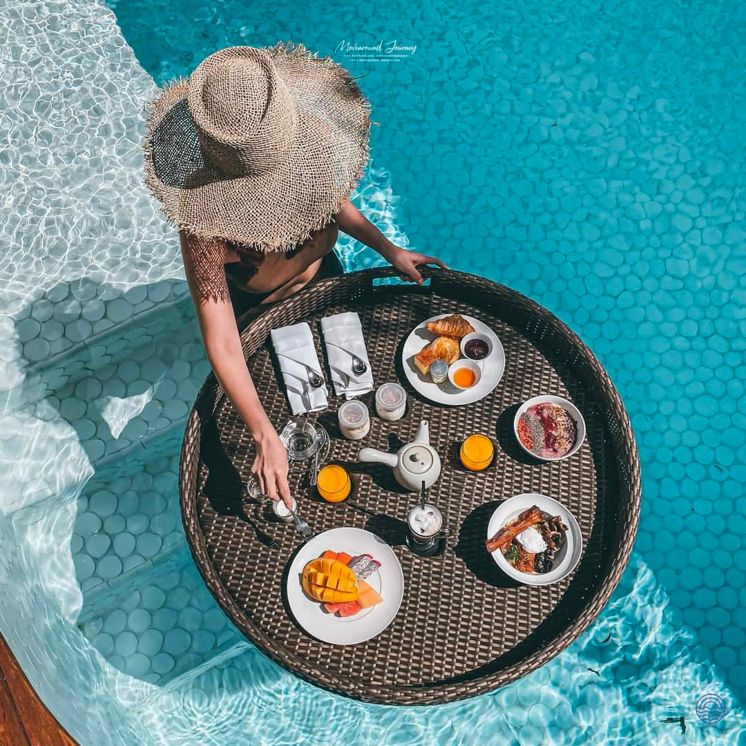 A woman in a straw hat enjoys a delicious floating breakfast in a private pool in Koh Samui.