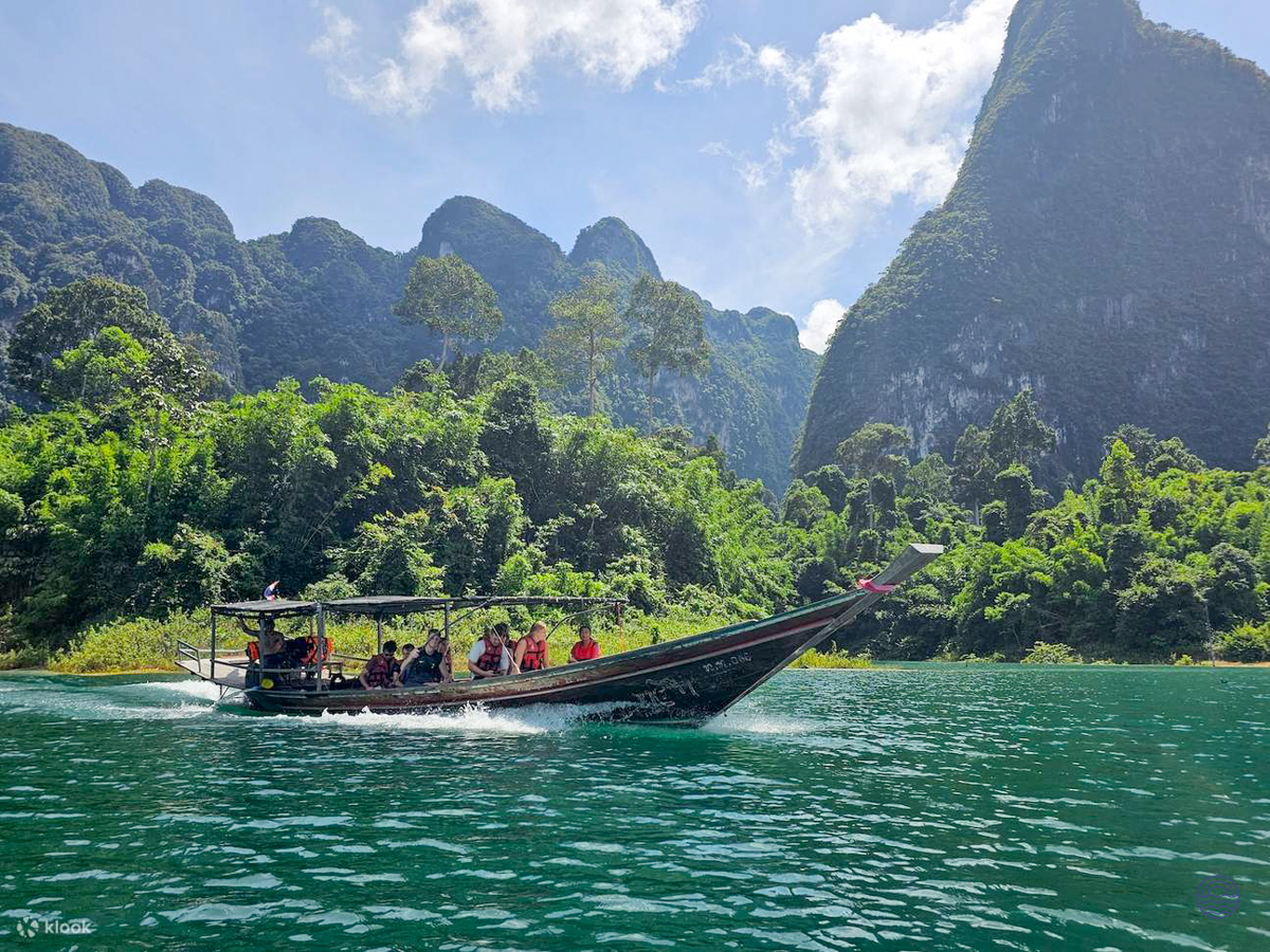 A longtail boat glides across the tranquil Chiewlan Lake, framed by stunning limestone karsts in Khao Sok.