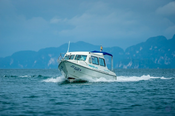 A white speedboat speeds across the tranquil waters of Koh Yao Noi, framed by majestic limestone karsts.