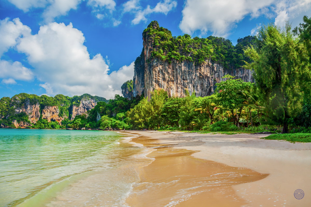 Majestic limestone cliffs rise above the pristine sandy beach and turquoise waters of Krabi.