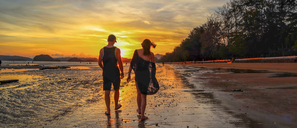 A couple enjoys a romantic sunset walk on the beautiful, reflective beaches of Krabi.