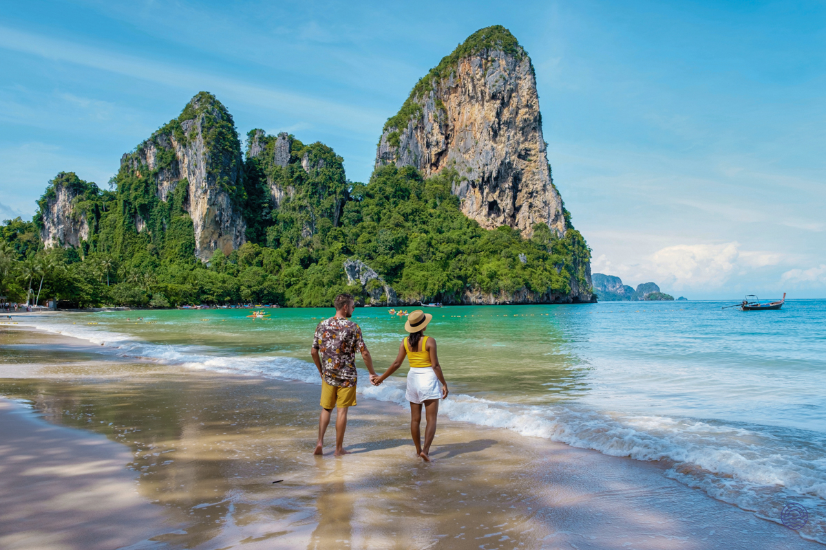 A romantic couple strolls hand-in-hand along the serene beach with majestic limestone cliffs in Krabi.