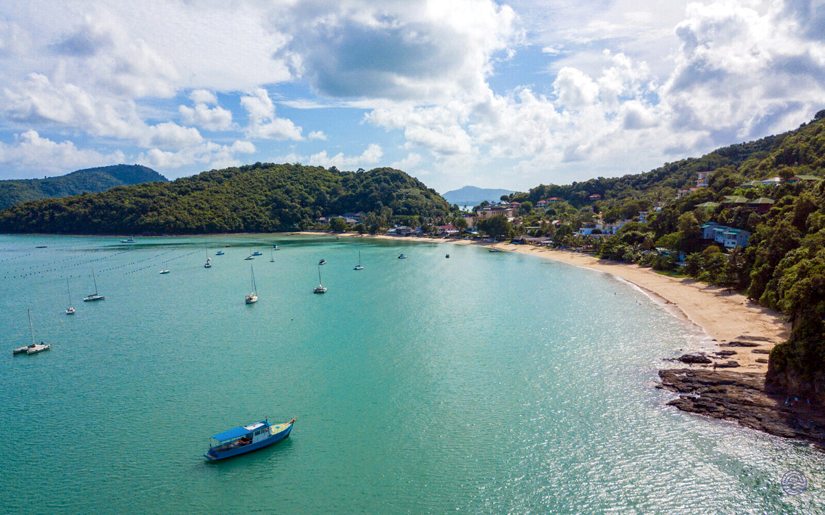 Beautiful tropical bay in Phuket with clear turquoise water, a sandy beach, and boats at anchor.