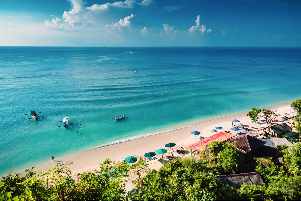 Stunning aerial view of a vibrant turquoise beach in Phuket with boats and lush green hills.