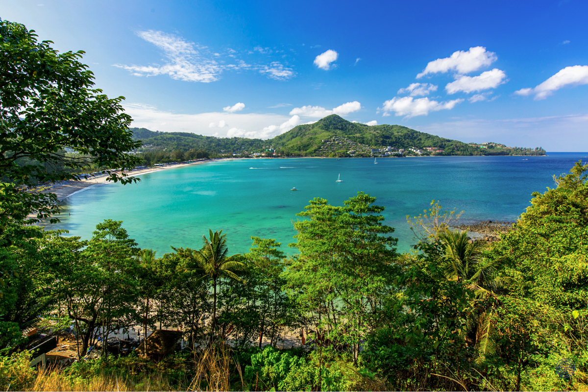Stunning panoramic view of a turquoise bay, sandy beach, and lush green hills in Phuket.